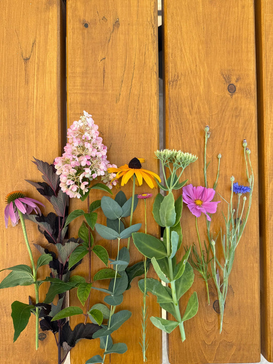 Frisch geschnittene Gartenblumen nebeneinander auf einem Holztisch: Sonnenhut, Rispenhortensie, Rudbeckia, Fetthenne, Cosmea und Kornblume