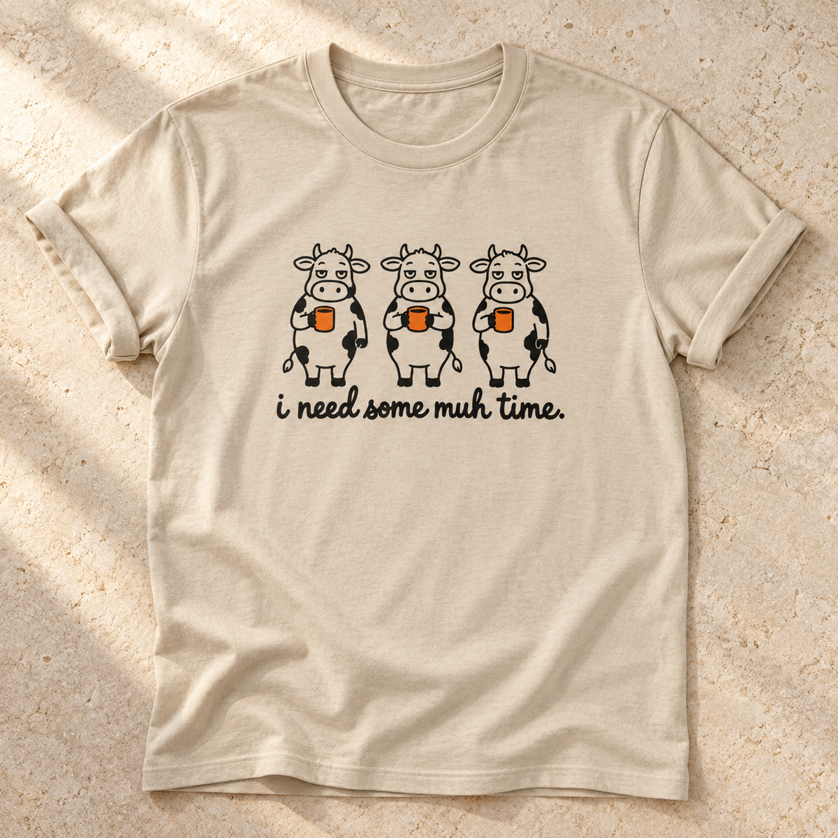 I Need Some Muh Time – Unisex Kuh-T-Shirt in Sand – natürliches Flatlay mit aufgekrempelten Ärmeln