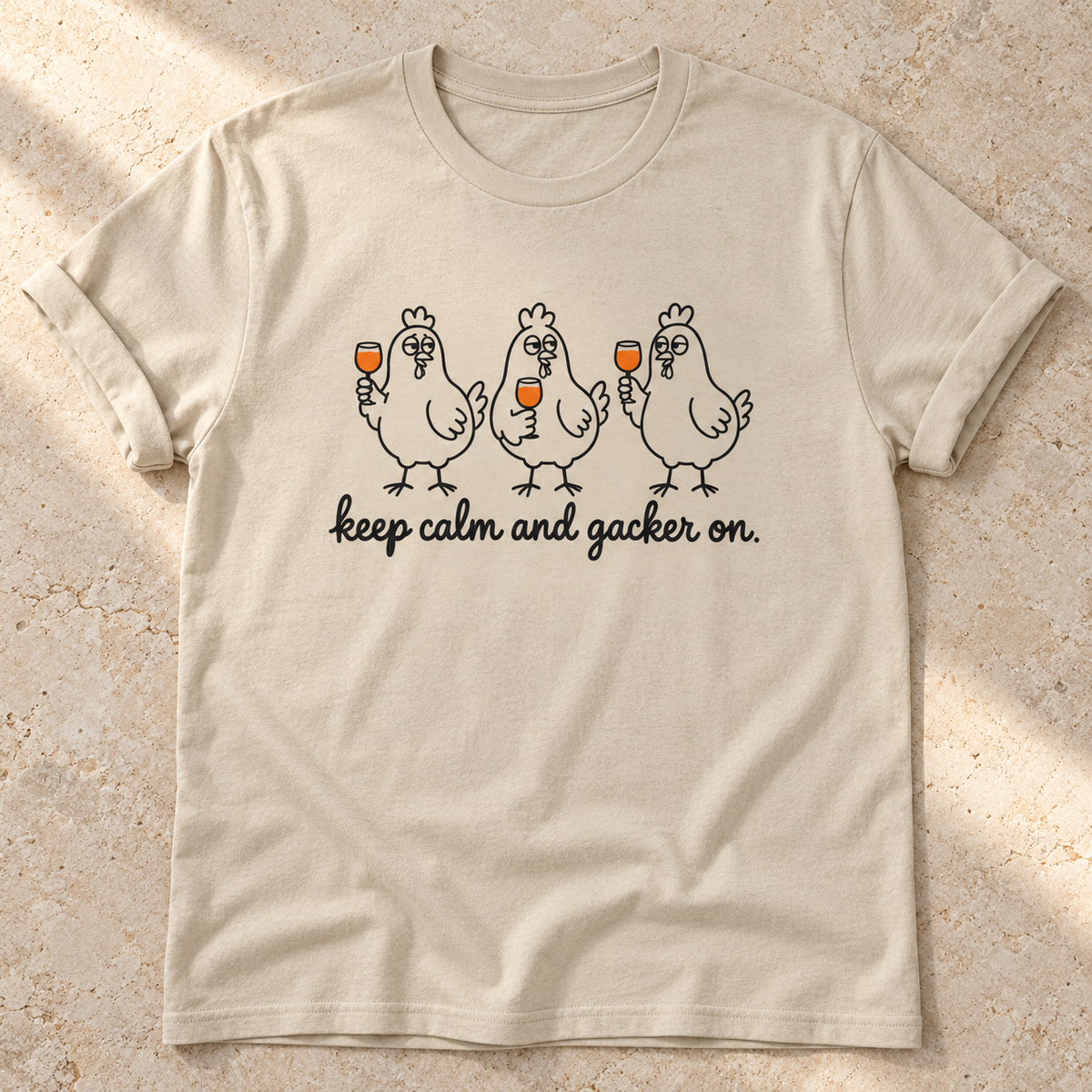 Keep Calm and Gacker On – Unisex Hühner-T-Shirt in Sand – natürliches Flatlay mit aufgekrempelten Ärmeln